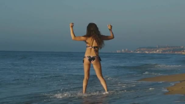 Красивая молодая женщина бежит в морскую воду на пляже, плескаясь и наслаждаясь береговой волной. Медленное движение — стоковое видео