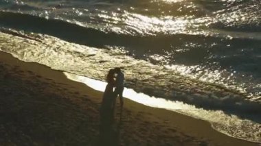 Elvoved çift günbatımı akşam sahil öp. Onlara yakın kumlu sahil şeridi üzerinde kırma dalgalar olarak çift öpücük