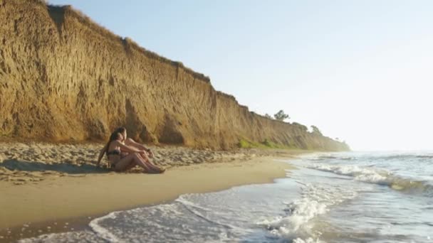 Feliz pareja joven se relaja en la playa de arena con altos acantilados de piedra arenisca. Concepto de luna de miel — Vídeo de stock