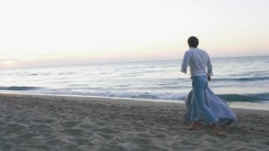 Genç Romantik Çift - uzun ışık elbise ve yakışıklı bir adam güzel kız şakacı kumsalda coastine çalışır