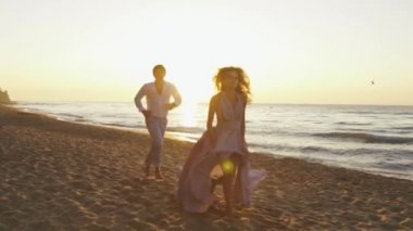 Genç Romantik Çift - uzun ışık elbise ve yakışıklı bir adam güzel kız şakacı kumsalda coastine çalışır