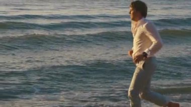 Sunsetin sarı günbatımı ışınları, plaj sahil şeridi boyunca çalışan yalınayak delikanlı