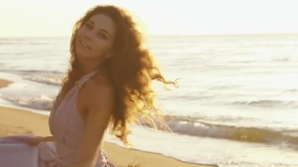 Charmiga flicka i långa ljus klänning löper lekfullt längs coastine på sandstrand vid gyllene timmen — Stockvideo