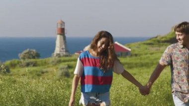 Genç çift holging eller birlikte, konuşuyor ve deniz kıyısı cliff fenerinde yakınındaki gülerek yürür. Ağır çekim