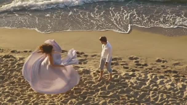Молодая романтическая пара - красивая девушка в длинном светло-розовом платье танцует на песчаном пляже для своего парня. Страстный момент развлечения — стоковое видео