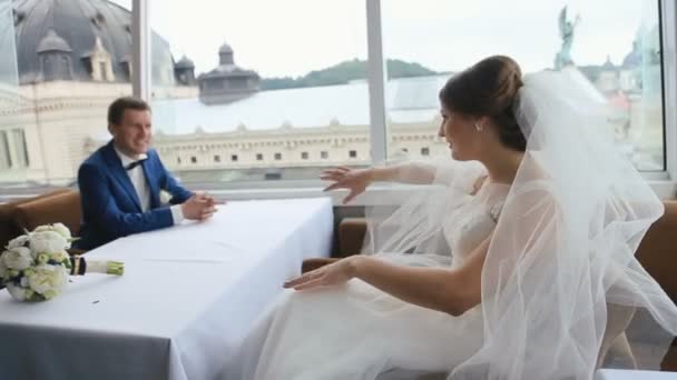 Feliz joven novia y novio en el amor sentado y posando en un café con vista panorámica de la ciudad. Concepto día de boda — Vídeo de stock