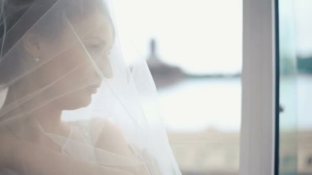 Close-up rosto de linda noiva loira pensativo coberto de véu transparente assistindo a paisagem urbana incrível na janela no café de luxo — Vídeo de Stock