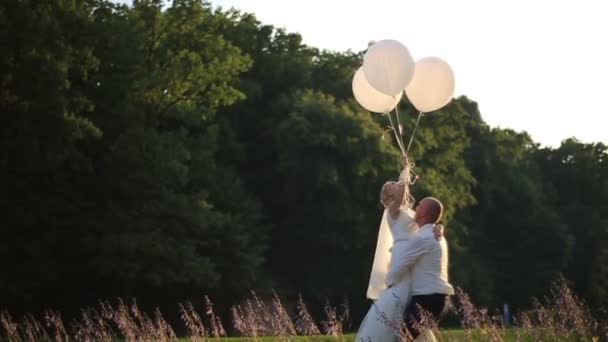 Sensuella ögonblick av kärlek. Lycklig brudgum carryes i händerna brud med ballonger. Solig sommar fältet bakgrund — Stockvideo