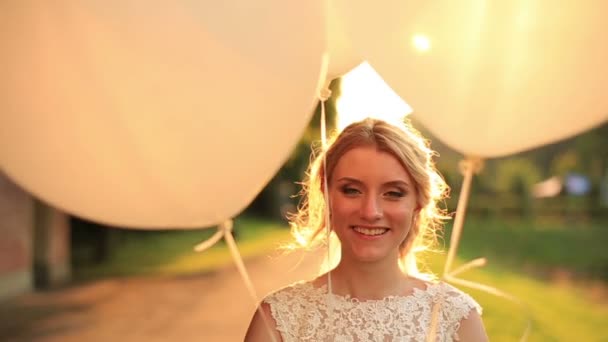 Nahaufnahme einer jungen schönen blonden Braut mit Luftballons, die glücklich lächelnd bei Sonnenuntergang im herbstlichen Park stehen — Stockvideo