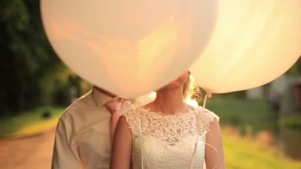 Happy young newlyweds with balloons making funny faces and laughing on sunset background in the autumn park — Stock Video