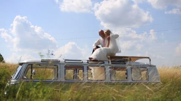 Noiva e noivo no topo do ônibus retro no campo de verão ensolarado. Dia de casamento incomum — Vídeo de Stock