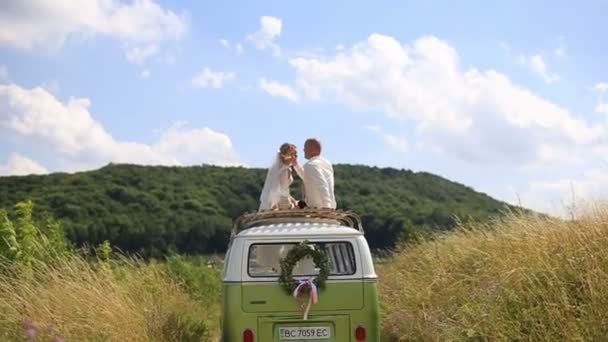 Feliz joven recién casados novia y novio en la parte superior del autobús de la boda Rerto en el campo de verano soleado. Tierno momento de amor — Vídeo de stock