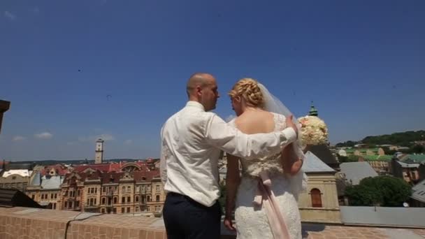 Щаслива розкішна наречена і стильний наречений з справжніми емоціями на даху з видом на старі міські будівлі міський пейзаж — стокове відео