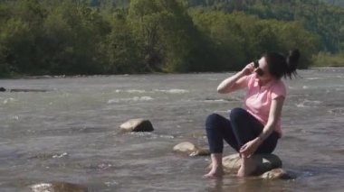 Duygusal telefonla konuşurken ve gülümseyen güneş gözlüklü genç çekici esmer kız. Dağ nehir arka plan