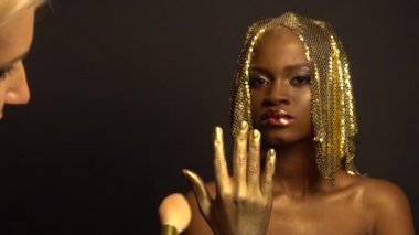 Makyaj işlemi close-up. Gerçeküstü altın Afro-Amerikan modeli ile parlak parıltı makyaj ve altın parlak saç stilist çekim için hazırlanıyor. Siyah stüdyo arka plan