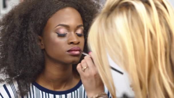 Vrouw make-up artiest toe te passen en sprankelende gouden make-up op fantastische zwarte Afrikaanse Amerikaanse vrouwelijke model te corrigeren. Schoonheid en glamour concept — Stockvideo