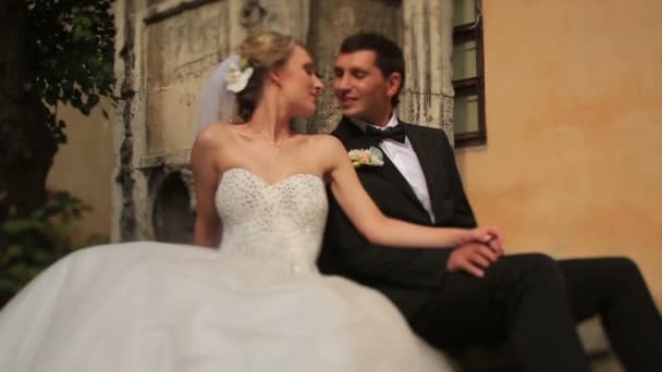 Hermosa novia rubia recién casada y novio guapo besándose frente al antiguo edificio barroco en Lviv. Día de la boda soleado, momento tierno — Vídeo de stock