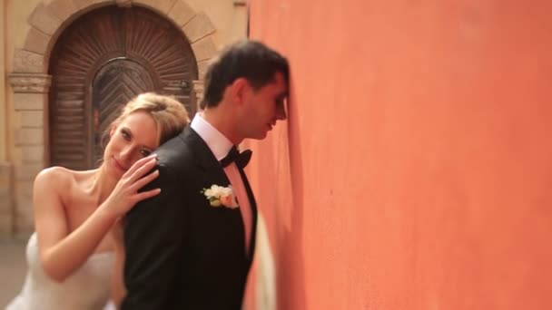 Beautiful happy blonde bride touched lovingly her thoughtful groom. Sunny Lviv historical center on background — Stock Video