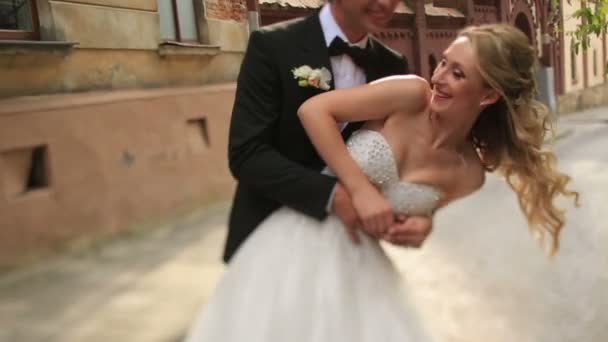 Happy groom spinning and kissing his beautiful blonde bride in front of an ancient christian church in Lviv. Charming newlyweds having fun together — Stock Video