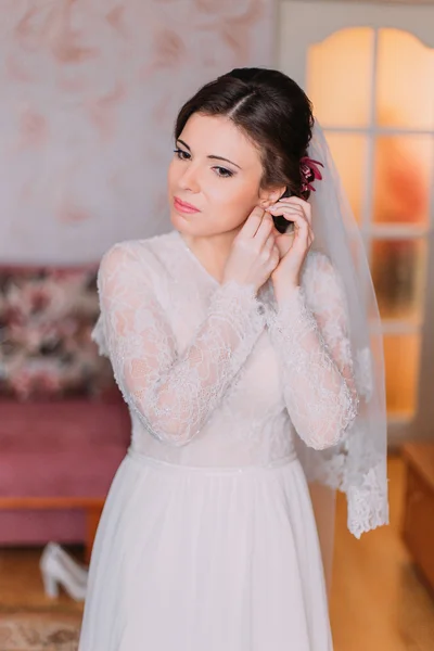 Retrato de novia encantadora en vestido de novia. Hermosas mujeres jóvenes vistiendo sus pendientes preparándose para la ceremonia — Foto de Stock