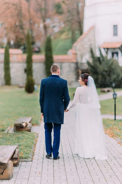 Charmiga nygift par på bröllop dag promenader utomhus på vacker grön park. Bakifrån — Stockfoto