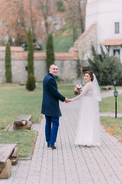 Affascinante coppia di sposi il giorno del matrimonio passeggiando all'aperto sul bellissimo parco verde — Foto Stock