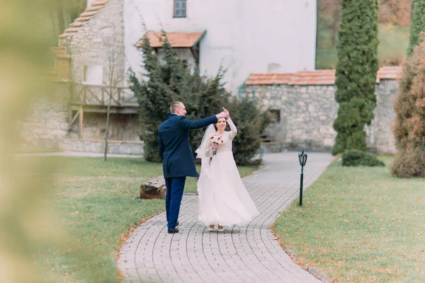 Charmantes Brautpaar tanzt am Hochzeitstag auf begrünter Parkstraße — Stockfoto