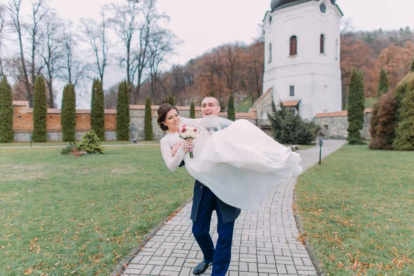 Par de recién casados apasionados felizmente caminando en hermoso parque verde. Amoroso novio mantener a su nueva esposa en las manos —  Fotos de Stock