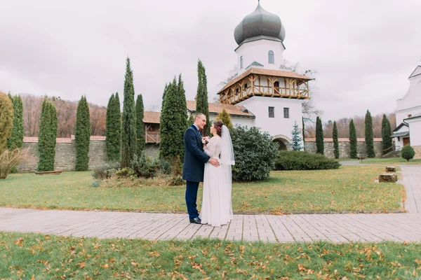 Vášnivé novomanželé objímat v romantické zeleného parku poblíž starožitný klášter — Stock fotografie