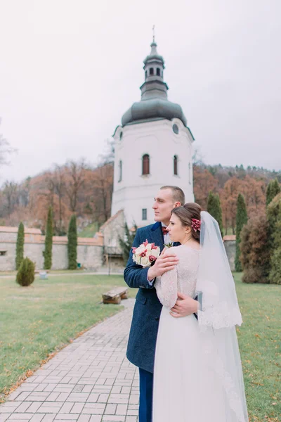 Красивий наречений ніжно обіймає свою нову дружину в зеленому парку старого монастиря — стокове фото
