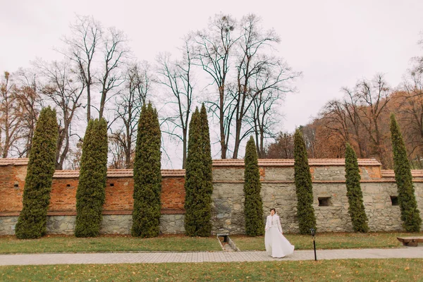 Okouzlující mladá nevěsta v kanárném plášti a kožešinové bundě na cestě v podzimním parku uvnitř opevněných hradních zdí — Stock fotografie