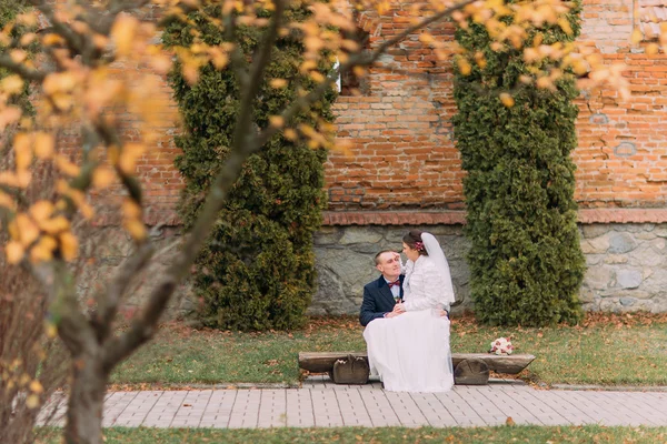 Feliz pareja de recién casados sentados en el banco en el parque teniendo una dulce charla — Foto de Stock
