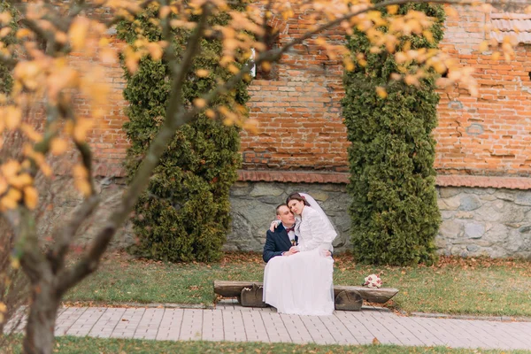 Felice coppia di sposi seduti sulla panchina nel parco autunnale. Sposa è appoggiato al suo nuovo marito spalla — Foto Stock