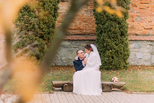 Feliz casal recém-casado sentado no banco no parque de mãos dadas — Fotografia de Stock