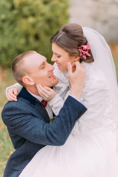 Feliz pareja recién casada al aire libre. Elegante novia sentada sobre las rodillas de su guapo nuevo marido — Foto de Stock