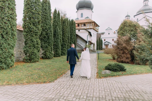 Красивий наречений гуляє зі своєю нареченою у відвертій весільній сукні в романтичному осінньому парку античного монастиря — стокове фото