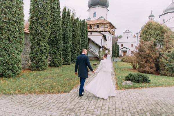 Красивий наречений гуляє зі своєю нареченою у відвертій весільній сукні в романтичному осінньому парку античного монастиря — стокове фото