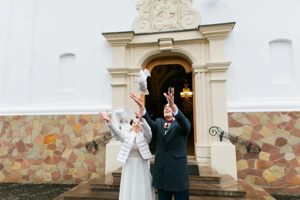 Casal recém-casado liberando pombas para voar ao deixar a igreja após sua cerimônia de casamento — Fotografia de Stock
