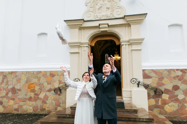 Casal recém-casado liberando pombas brancas ao deixar a igreja após sua cerimônia de casamento — Fotografia de Stock