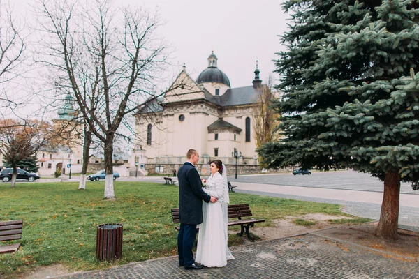 Vista panorámica de la pareja beaytiful recién casados tomados de la mano en el parque cerca de la antigua iglesia barroca — Foto de Stock