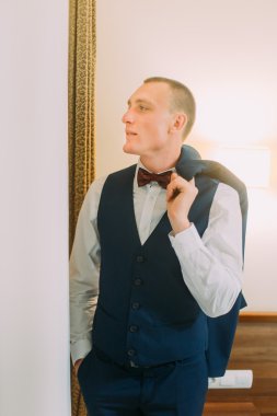 Mavi takım elbise giymiş yakışıklı genç atletik adam kapalı poz, omzunun üzerinde Blazer tutarak