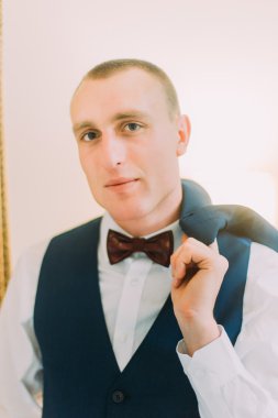 Yakışıklı genç atletik adam mavi takım elbise giymiş ve bow-tie kapalı poz, omuz üzerinde Blazer tutarak