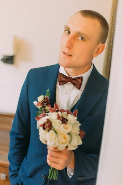 Atraente elegante vestido homem segurando elegante buquê de rosas em pé interior perto da porta — Fotografia de Stock