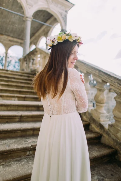 Vacker lantlig stil brud i lång vit brudklänning och blommig krans står tillbaka på trappan — Stockfoto