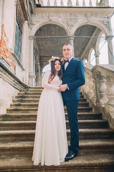 Suave noivo de mãos dadas com sua noiva bonita, enquanto ambos estão em escadas de pedra antiga. Retrato de comprimento total — Fotografia de Stock