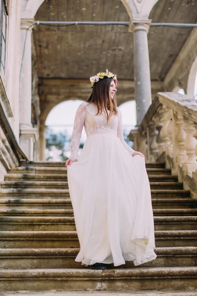 Γοητευτική νύφη στο μακρύ λευκό νυφικό και floral στεφάνι κατεβαίνοντας από την παλαιά πέτρινα σκαλοπάτια — Φωτογραφία Αρχείου