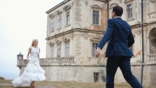 Heureux jeunes mariés qui courent et tombent dans les bras les uns des autres. Magnifique château médiéval arrière-plan — Video