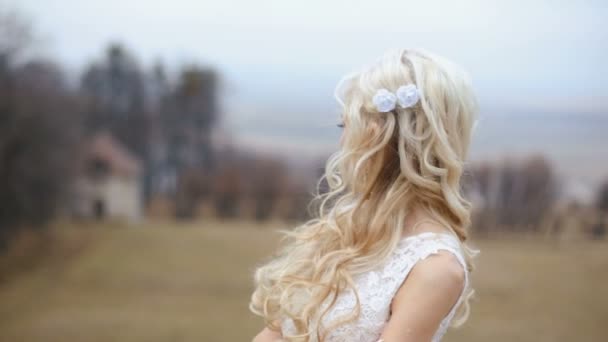 Belle mariée blonde élégante aux cheveux longs venteux posant sur le fond flou du château — Video