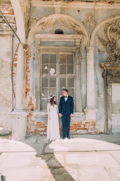 Glückliche Braut und Bräutigam, die einander in einem alten zerstörten Backsteinfenster eines alten Gebäudes anschauen — Stockfoto