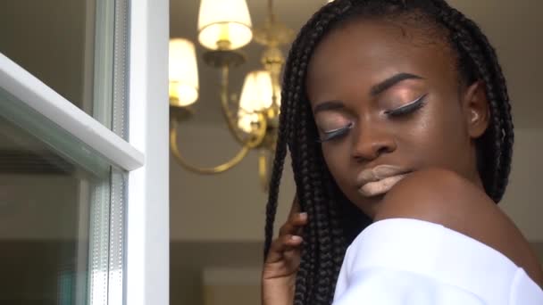 Närbild av vackra drömmande unga afroamerikanska kvinnan med flätad frisyr poserar på fönsterkarmen — Stockvideo